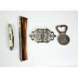 A silver belt buckle, a 1780 M Theresia coin made into a bottle opener, a silver edged comb, and a