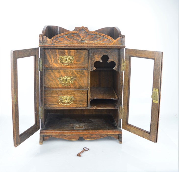 An oak smokers cabinet with three interior drawers with original key and glass fronted doors