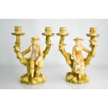 A pair of Royal Worcester candelabra modelled as figures seated on a tree stump forming two candle