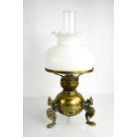 A Victorian brass oil lamp, the reservoir raised on three griffin form brass feet, with a white