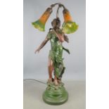 An Art Nouveau style lamp with a female figure in aged brass standing on a decorative base of leaves