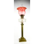 A 19th century paraffin lamp with pink glass shade, raised above a Corinthian column form brass
