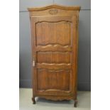 A French single door oak armoire, with shaped and carved top, above a panelled door, enclosing