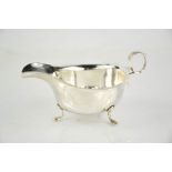 A silver sauce boat with shaped edge, acanthus design to the handle, raised on three feet,