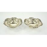 A pair of silver dishes, pierced and embossed with decoration, and raised on three ball feet,