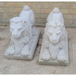 A pair of reconstituted stone lions leaning on rams heads and raised on a plinth, 60cm by 29cm by