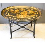 A Chinoiserie black lacquered table, the top of oval form decorated with figures and houses in