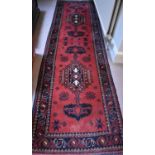 A Middle Eastern red ground runner decorated with dark blue borders and stylised motifs, 297cm by