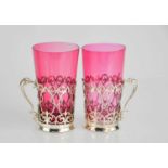 A pair of silver and cranberry glass tea holders or podstakannik, the silver holders pierced with