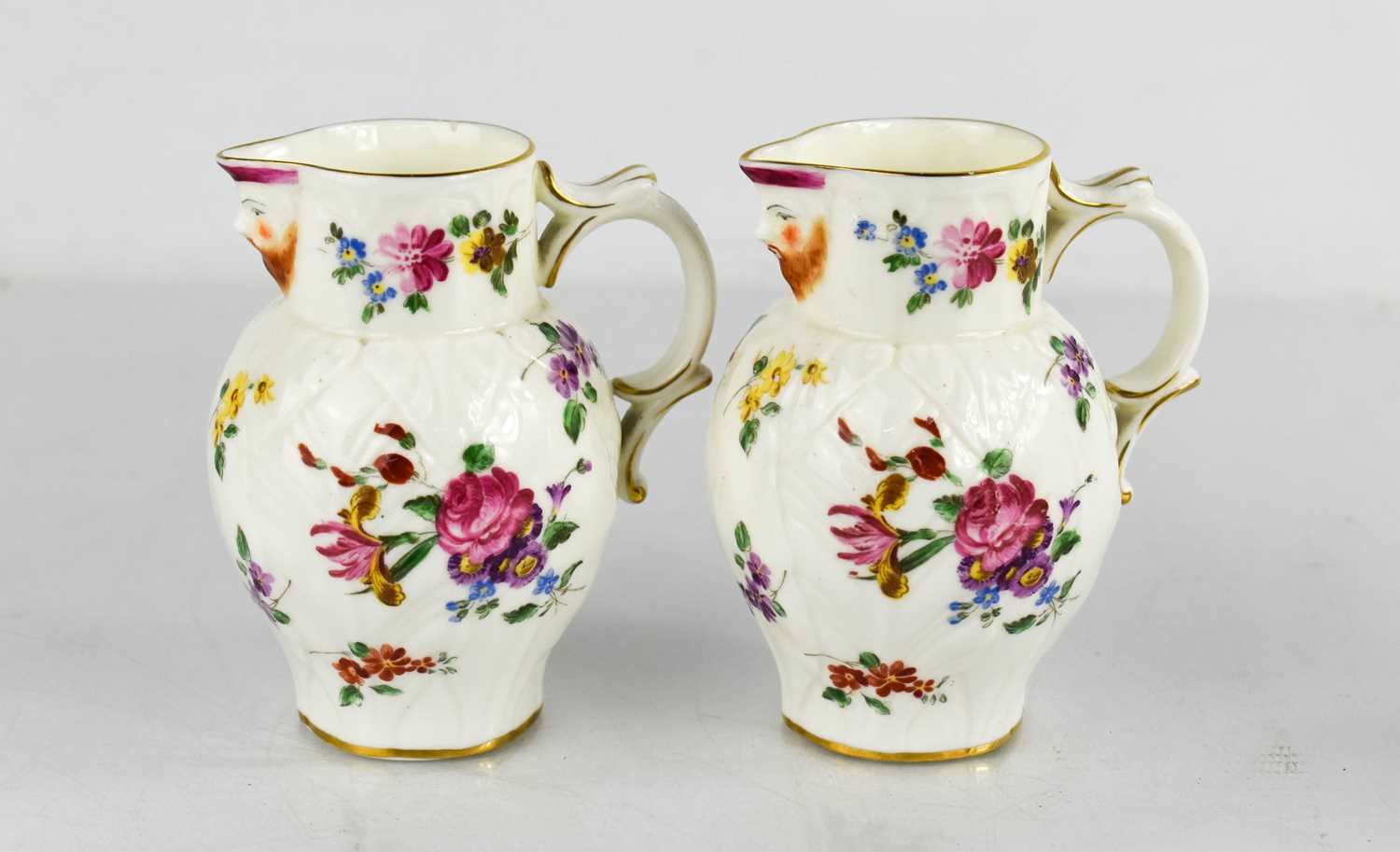 A pair of Royal Worcester leaf moulded jugs with painted roses, face mask spouts and scroll handles,