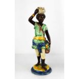 A 19th century majolica figure of an African boy holding a basket in one hand and supporting a