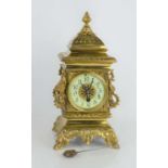 An early 20th century brass mantle clock with enamelled dial, acorn finial and animal mask hoop