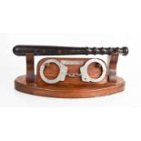 A presentation truncheon with handcuffs in wooden stand, presentation engraved to 'T. S. Marley,