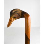 A treen walking cane, the handle carved in the form of a duck head, inset with glass eyes, 130cm