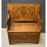 An oak monks bench, the underside lid / back carved with a shield and scroll work.75cm high by