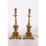 Pair of gilded metal candlestick table lamps, the ornate stems supported by a trio of cherub