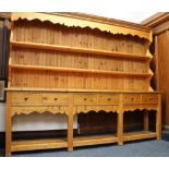 An oversize pine Welsh dresser with shaped pelmet above two long shelves over six drawers and open