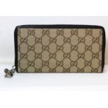 Gucci zip around wallet in GG canvas with brown leather trim and white metal zip pull.