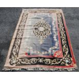 Eastern rug with central floral lozenge over faded blue ground, black and pink floral border,