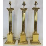 Three large modern brass table lamps of Corinthian column form on square plinth bases, each 67.5cm