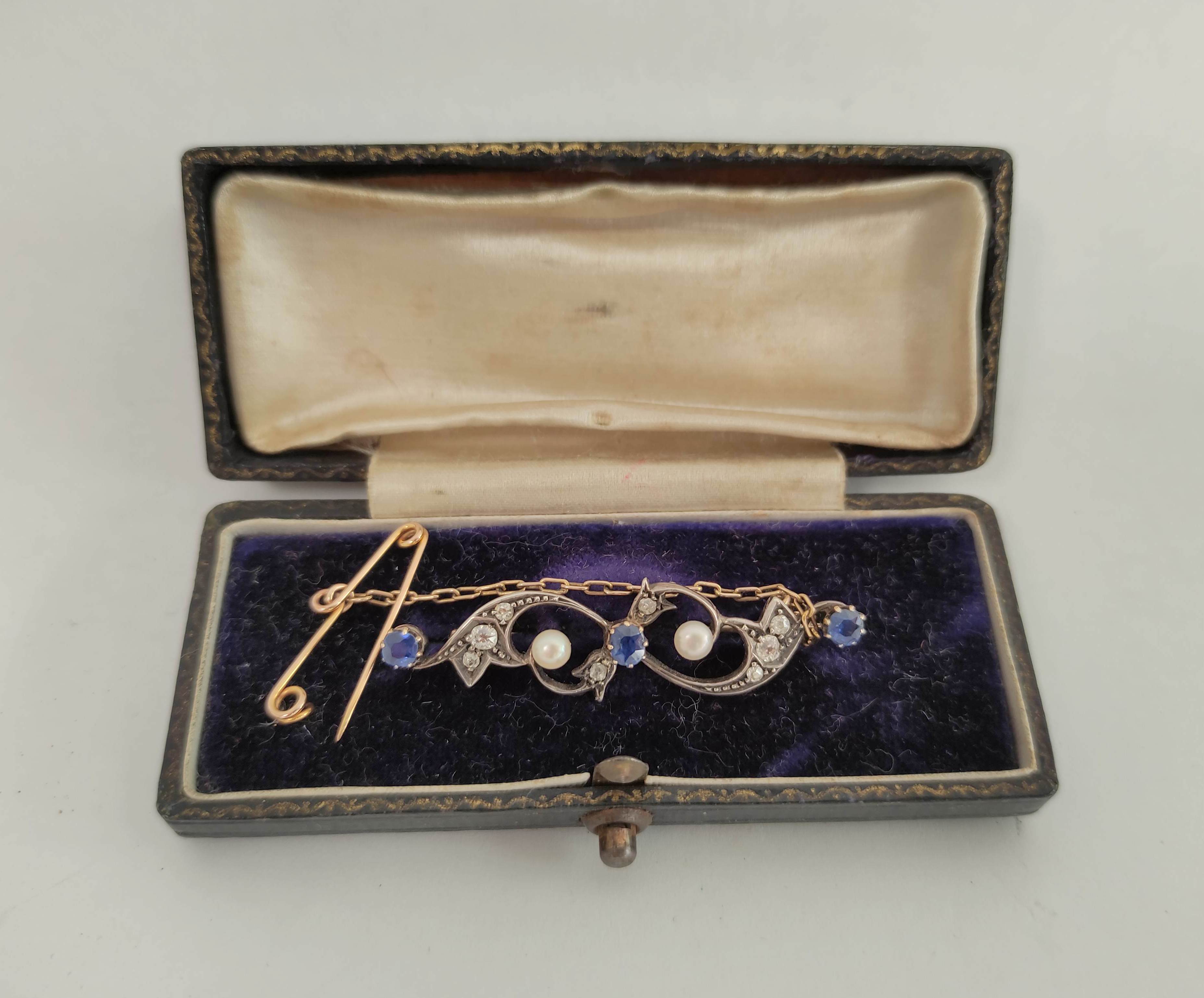 Edwardian gold brooch with scrolls of three sapphires and diamonds in gold and silver.