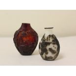 Two antique Chinese snuff bottles to include a dark red carved amber bottle decorated with reliefs