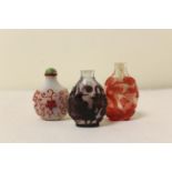 Three Chinese overlay glass snuff bottles, the first of purple glass constructuion bearing a