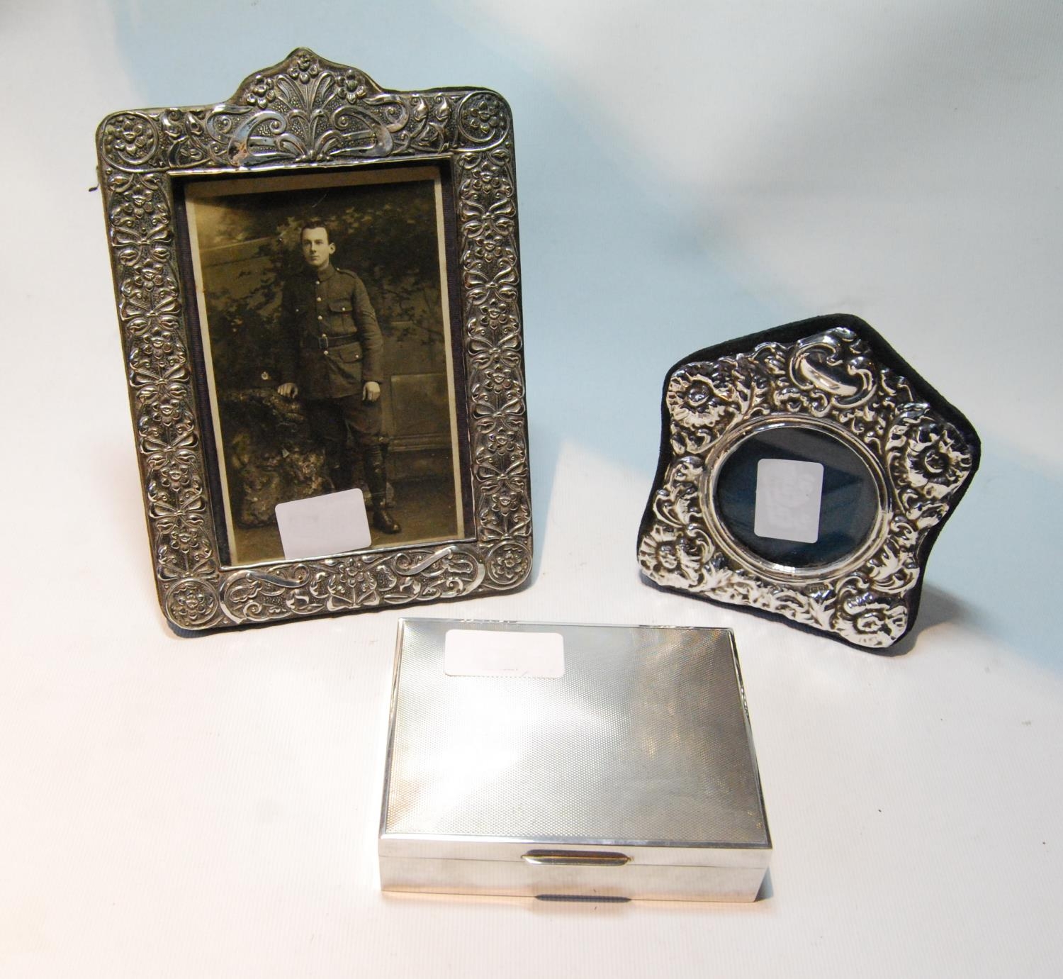 Silver engine-turned cigarette box and two embossed silver photograph frames.  (3)