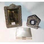 Silver engine-turned cigarette box and two embossed silver photograph frames.  (3)