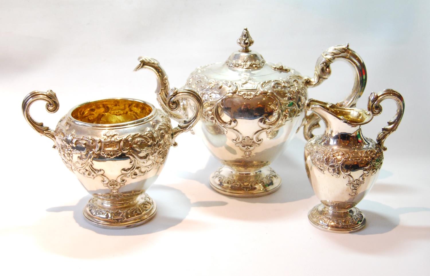 Silver three-piece tea set of half ovoid shape, embossed with rococo scrolls, by William Mortimer or