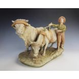 A Royal Dux model of a boy herding cattle, in pastel tones and gilt shot enamels, pink triangular