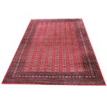 A Bokhara carpet, the central panel with repeating geometric gulls upon a vibrant red ground, within