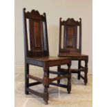A pair of 18th century oak hall chairs, each with a panel back over a board seat, raised upon turned