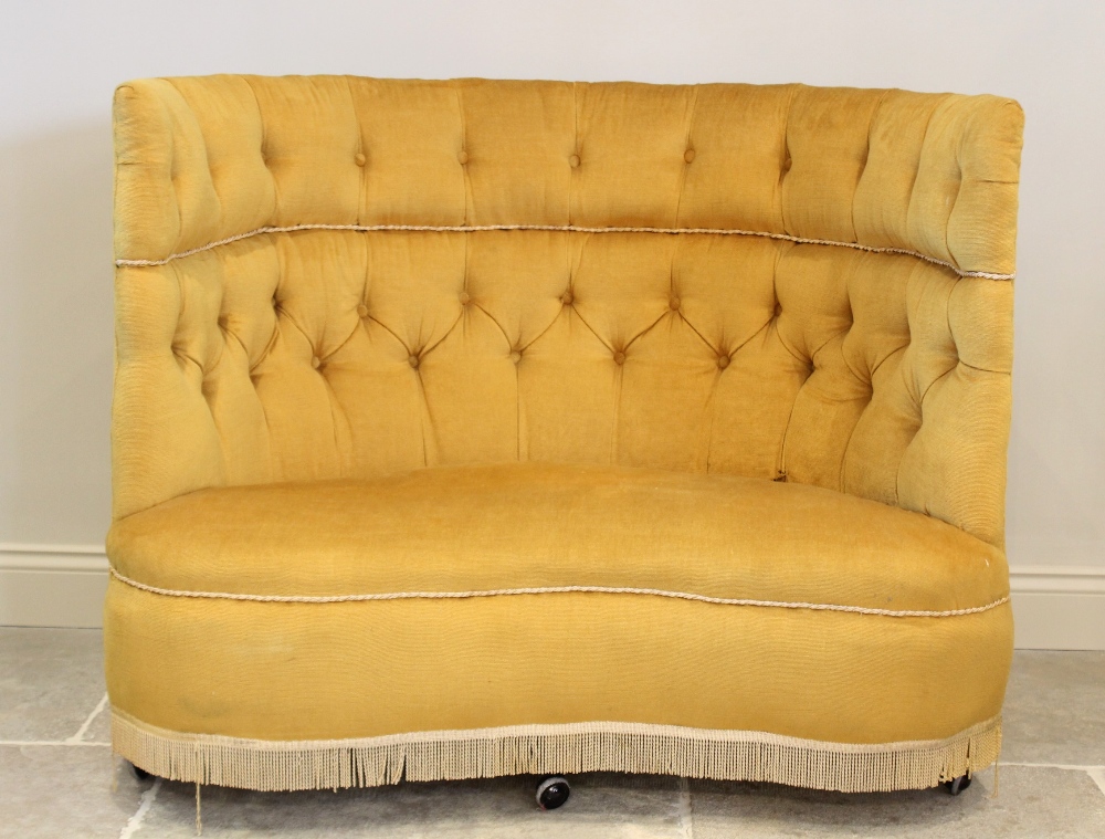 An early 20th century button back love seat, upholstered in yellow velour, the wrap around high back