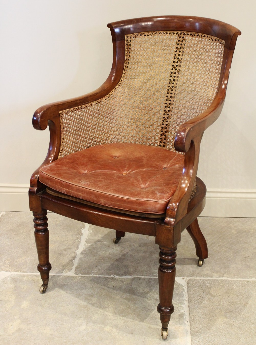 A late Regency mahogany bergère tub chair, the shaped back extending to down swept arms enclosing