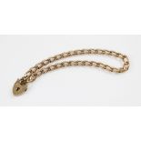 A 9ct gold curb link charm bracelet, 18cm long, suspending a 9ct gold heart-shaped padlock fastener,