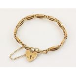 A 9ct gold gate link bracelet, 18cm long, suspending a 9ct gold heart-shaped padlock fastener,