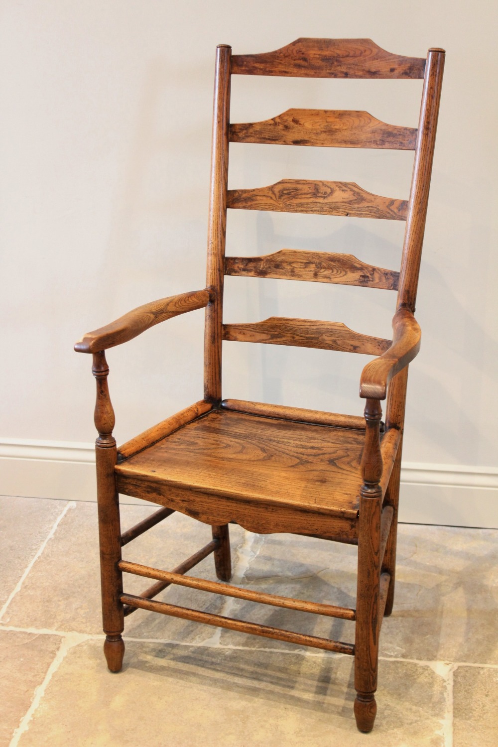 An early 19th century ash and elm ladder back country chair, the five rung back above out swept arms