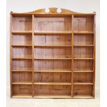An early 20th century honey oak open bookcase, the shaped pediment with a shield shaped motif