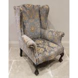A George II style wing back fireside armchair, early 20th century, covered in embossed foliate