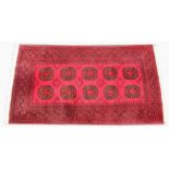 A Bokhara style rug, with ten octagonal medallions upon a vibrant red ground, 210cm x 110cm