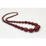 A cherry amber bead necklace, comprising fifty-seven polished oval beads measuring between 8mm x 6mm