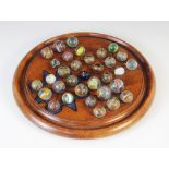 A 19th century mahogany solitaire board, with thirty-three assorted marbles of various design,