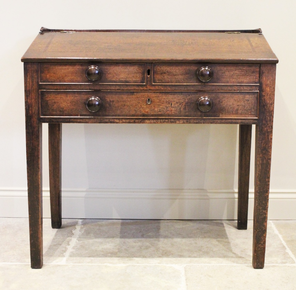 A George III oak clerks desk, the three quarter galleried top above a cross banded hinged slope,