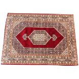 A Persian pattern silk work rug, the central angular medallion upon a vibrant red ground, within