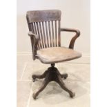 An early 20th century beech wood revolving desk chair, the lath back above a board seat, raised upon