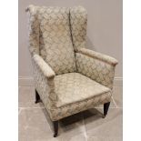 A late 19th century/early 20th century wing back armchair, covered in stylised foliate fabric, the