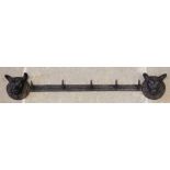 A cast iron wall mounted coat or hat rack, the five hook rail applied to the wall by a pair of