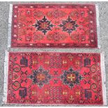 Two small Persian pattern wool rugs, each with a pair of geometric medallions upon a red ground, the