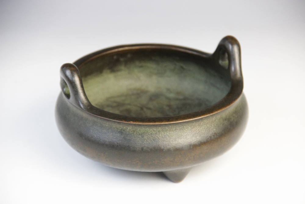 A Chinese bronze censer, of squat bulbous form with loop handles raised on three tapered feet,